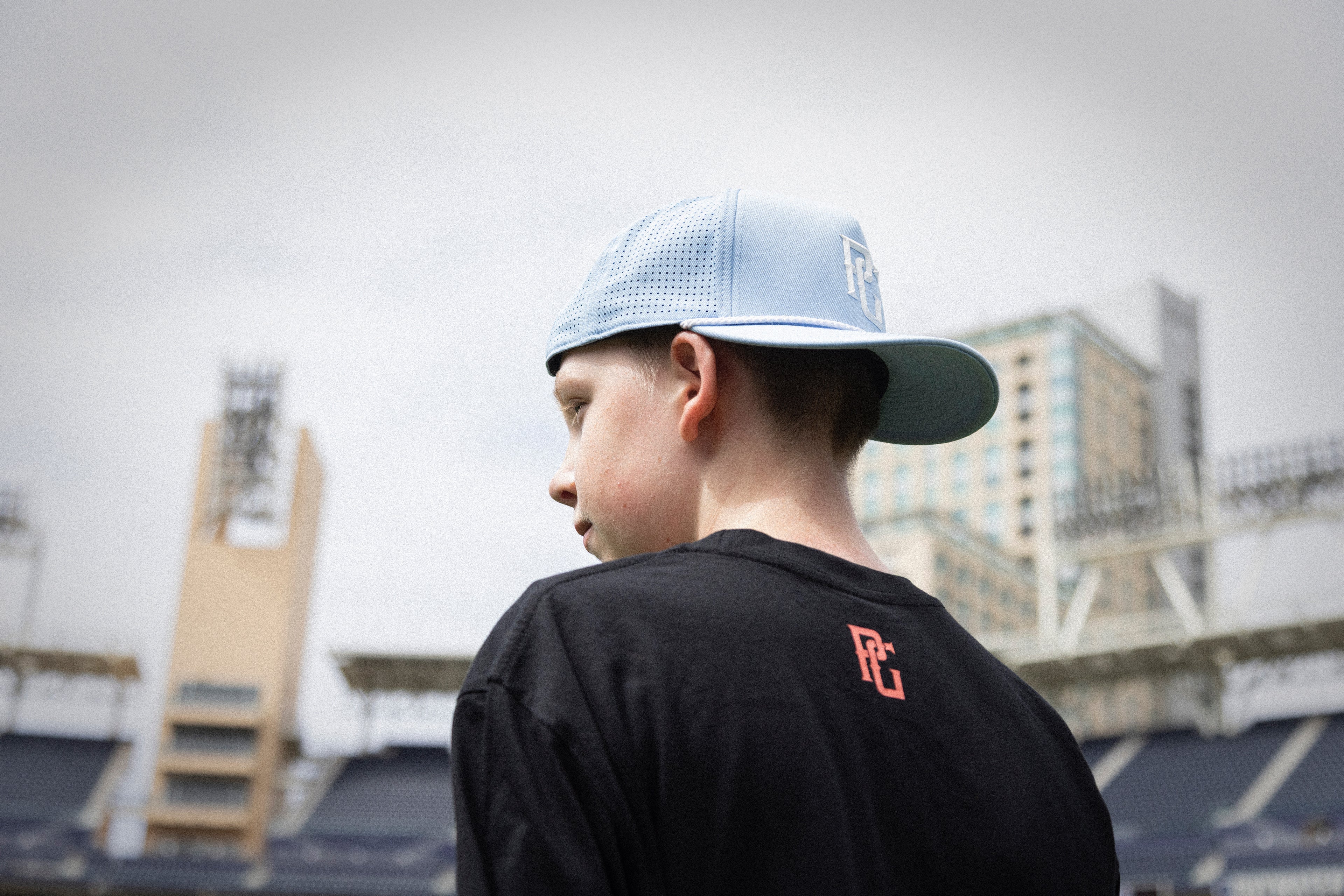 Person wearing a black t-shirt with a red logo and a light blue cap, standing in an outdoor setting.