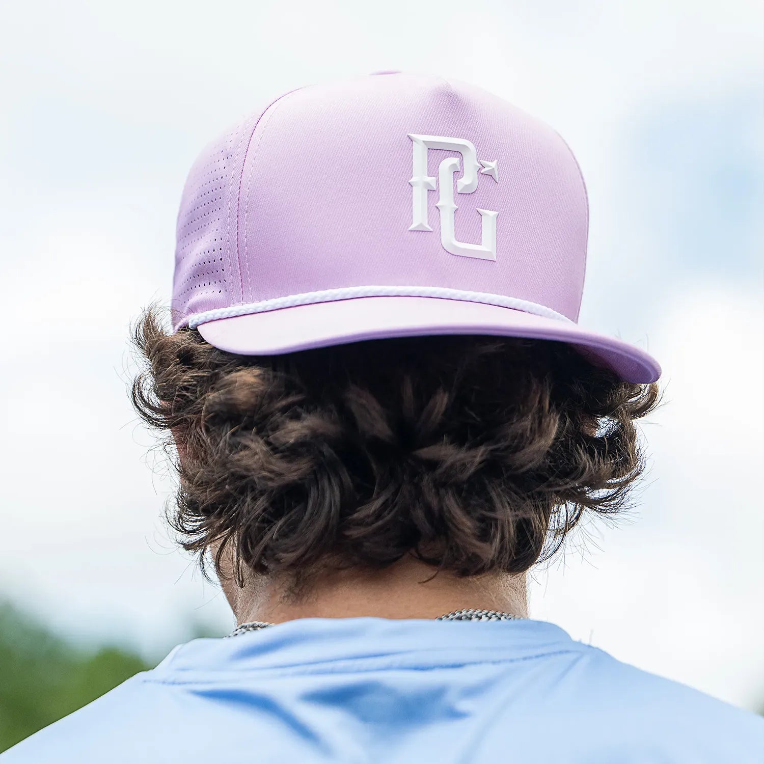 Person wearing a light purple cap with a logo, looking away from the camera.